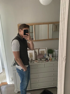 Svart dunväst med ståkrage - Snygg svart dunväst med ståkrage och diskret quiltad design. Västen har en smal passform och stängs med dragkedja framtill. Perfekt att slänga över en t-shirt eller hoodie för en stilren look.