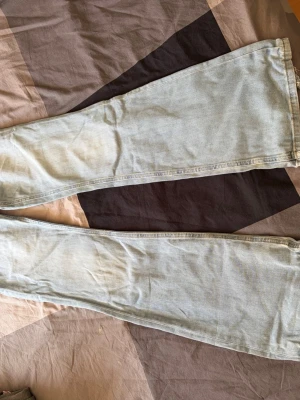 Ljusblåa utsvängda jeans - Säljer ett par ljusblå jeans med utsvängda ben. Jeansen har klassisk femficksdesign och är tillverkade i denim. Perfekta för dig som gillar en retro och avslappnad stil.