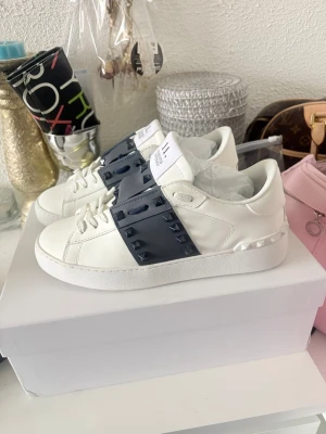 Valentino opens - Skorna är köpta för 5 499kr.                                                  Säljer ett par vit blå Valentino opens dam med en bred navy blue rand. Skorna har en klassisk låg siluett, vita snören och detaljerade sömmar. Tillverkade i slätt läder för en clean och modern look. Det är strl 40 men jag har vanligtvis 38,5 i mina skor och de passar mig bra. Använda 1 gång med minimala smutsfläckar som knappast syns. Hör av vid frågor🥰 