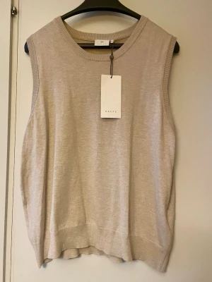 *NY*Beige stickad väst i stl XXL från Kaffe - Ny med lapp. Kalizza knit slipover.  I färgen feather gray melange.  Material: 80% Viskos, 20% Nylon. Tunnstickad i mjuk viskos. Ord pris: 399 sek, Pris nu: 150 sek. Ärmlös stickad väst för dam med avslappnad passform och klassisk rund halsringning. Ribbstickade kanter ger extra komfort och stil vid vardagsbruk. Perfekt att styla över en skjorta eller t-shirt för en trendig lager-på-lager-look. 
