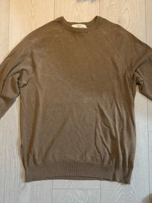 Beige rundhalsad tröja från Lyle & Scott - Klassisk beige tröja från Lyle & Scott med rund halsringning och ribbade muddar vid ärmslut och nederkant. Tillverkad i ett mjukt och tunt material som passar perfekt för lager på lager. Enkel och stilren design som funkar till det mesta.