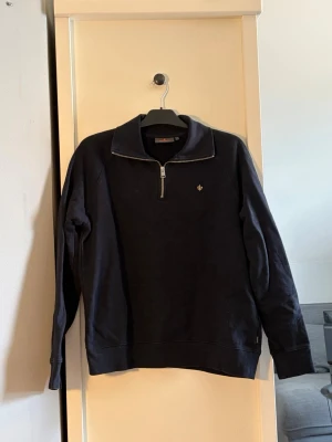 Marinblå quarter zip från Morris  - Stilren marinblå tröja från Morris med halv dragkedja och liten broderad logga på bröstet. Tröjan har hög krage, långa ärmar och är tillverkad i mjukt material. Perfekt för en avslappnad men snygg look.