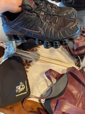 Nike Shox TL svarta sneakers - Svarta Nike Shox TL sneakers med ikonisk fjädrande sula och mesh- och syntetöverdel. Snygga detaljer i svart och rött, med diskret Swoosh på sidan. Skorna har en sportig vibe och passar perfekt för dig som gillar streetwear och unika siluetter.