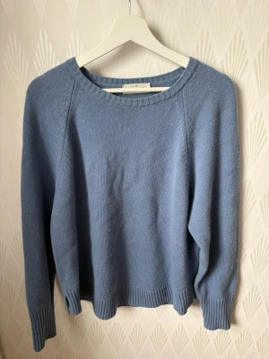 Blå stickad tröja från Arket - En stilren blå stickad tröja med rund halsringning och långa ärmar. Tröjan har ribbade muddar vid ärmslut och nederkant, vilket ger en snygg och avslappnad look. Perfekt för lager-på-lager och enkel att matcha med jeans eller kjol.