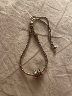 Pandora silverarmband med berlocker - Snyggt silverfärgat armband från Pandora med flera glittrande berlocker. Armbandet har en ormkedja och detaljerade lås med Pandora-logga. Perfekt accessoar för att lyfta din stil med en personlig touch.