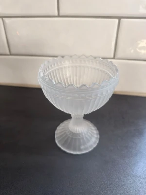 Frostad Marimekko  glasskål på fot - Säljer en elegant Marimekko glasskål på fot i frostat glas med räfflat mönster och vågig kant. Perfekt som dessertskål eller till smågodis. Skålen har en klassisk form och är genomskinlig med fina detaljer längs kanten och foten.