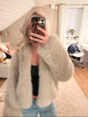 Beige fluffig pälsjacka - Säljer en supermjuk och fluffig beige pälsjacka med rak passform och långa ärmar. Jackan är kortare i modellen och har en stilren look som passar perfekt till kalla vinterdagar. Materialet är fuskpäls och jackan är utan synliga knappar eller dragkedja.