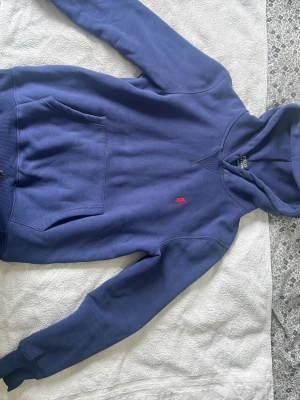 Marinblå hoodie från Polo Ralph Lauren - Snygg marinblå hoodie från Polo Ralph Lauren med klassisk röd broderad logga på bröstet. Hoodien har huva, magficka och ribbade muddar vid ärmslut och nederkant. Perfekt för en avslappnad och stilren look.
