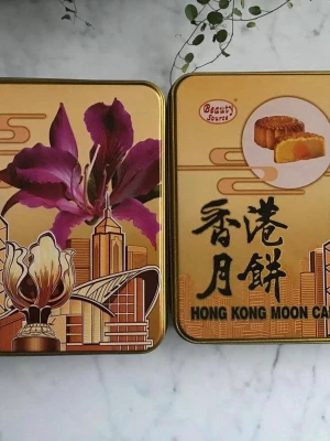  plåtburk - Säljer en fyrkantig plåtburk i guld med motiv av en lila blomma och stadssilhuett samt texten 'Hong Kong Moon Cake'. Perfekt för förvaring eller dekoration. Burken har lock och är tillverkad i metall. Ny skick 