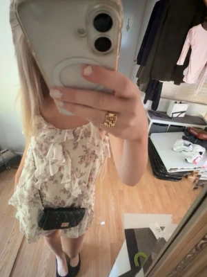 Blommig volangklänning i ljusa toner - Supersöt kort blommig klänning i ljusa färger med volangdetaljer och fint mönster. Jätte fin till skolavslutning eller att ha nu till sommaren Klänningen är ärmlös och har en luftig passform, perfekt för varma dagar. Materialet känns lätt och flowy, vilket ger en skön känsla.