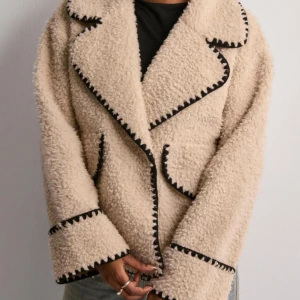 Beige teddyjacka med svarta detaljer - Säljer en beige teddyjacka. Jackan har två stora fickor framtill och en loose passform. Så snygg inför hösten och vintern!!