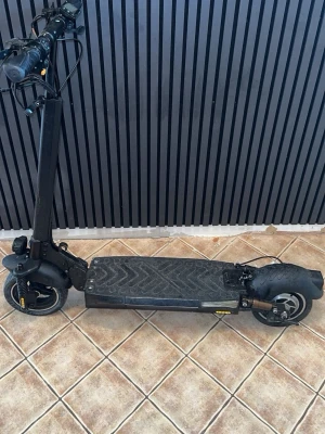 Svart elscooter med stora hjul - Elektrisk scooter i svart med bred fotplatta och stora hjul. Scootern har digital display på styret, handbroms och robust ram i metall. Perfekt för att ta sig fram snabbt i stan. Laddningsuttag och reflexdetaljer finns på sidan.