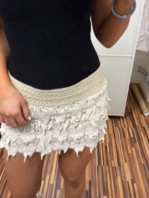 Beige virkad minikjol med volang - Superfin beige kortkjol med virkade detaljer och volangkant. Kjolen har en bred, elastisk midja och är perfekt för dig som gillar en boho-stil. Materialet känns som bomull och kjolen har en ljus, fräsch ton.