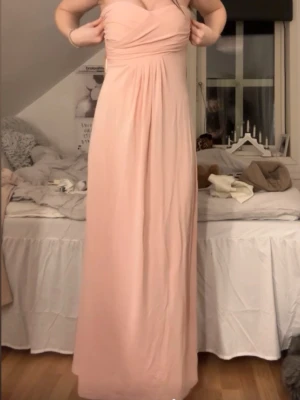Ljusrosa långklänning - Supersöt ljusrosa långklänning, perfekt för speciella tillfällen så som tillexempel bal. Materialet känns mjukt, troligtvis polyester eller liknande.