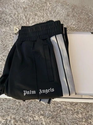 Palm Angels svarta mjukisbyxor - Säljer ett par Palm Angels byxor i storlek L i svart färg.  Byxorna är i bra skick men inte nyskick, med något mer slitage än nytt men fortfarande helt fina att använda och sitter bra. Inga större skador eller hål.  Har den klassiska Palm Angels-stilen som ger en snygg och trendig streetwear-look, perfekt till både vardag och mer stylade outfits.  Pris: 1899 kr Storlek: 
