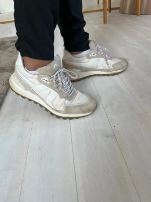 Vita sneakers från J.Lindeberg - Snygga vita sneakers från J.Lindeberg med beige detaljer och grov sula. Skorna har en mix av mocka och textilmaterial, klassisk snörning import och låg profil. Perfekta för dig som gillar stilrena och sport sopirerade sneakers.