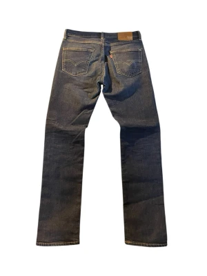 Levi's raka blå jeans | 511 | W33 L34 - Klassiska blå jeans från Levi's med rak passform och fem fickor. Jeansen har guldfärgade nitar och kontrastsömmar samt den ikoniska läderlappen bak i midjan. Tillverkade i slitstark denim med en tidlös look.