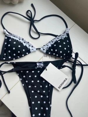 Oanvänd prickig bikini  - Supersöt svart bikini från Bershka med vita prickar och volangdetaljer längs kanterna på överdelen. Klassisk trekantsmodell med knyt både i ryggen och nacken samt på sidorna av underdelen. Både överdelen och unsderdelen är helt oanvända med prislappen kvar! Perfekt nu till sommaren!🩷🩷🩷
