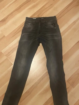 Svarta slim fit jeans från Replay - Säljer ett par svarta slim fit jeans från Replay, modell Anbass. Jeansen har klassisk femficksdesign, svarta sömmar och subtila slitningar för en cool look. Materialet är stretchigt för extra komfort och passform. Helt nya replay jeans använda 3 gånger.