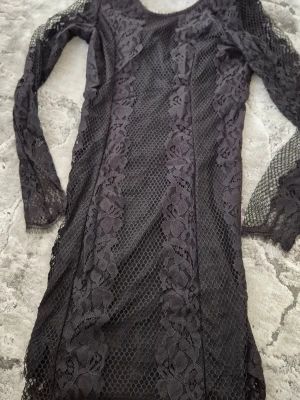 Svart spetsklänning från BikBok - Snygg svart kort klänning från BikBok i spets med blommigt mönster. Klänningen har lång ärm och figurnära passform. Perfekt för dig som vill ha en elegant och trendig look med fina detaljer.