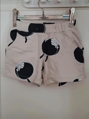 Beige Lindex shorts med glassar, storlek 98/104 - Säljer ett par beige shorts med härliga glassar, elastisk midja och sidofickor. Perfekta för varma dagar och har en avslappnad passform. Materialet känns mjukt och bekvämt, i bomull.                     Storlek 98/104.                                                         Mycket fint skick! Djur och rökfritt hem 