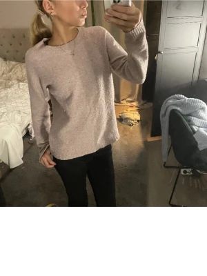 Ljusrosa stickad tröja - Mysig ljusrosa stickad tröja med rund halsringning och långa ärmar. Tröjan har en enkel, rak passform och ribbstickade muddar vid ärmslut och nederkant. Perfekt för lager på lager och en avslappnad stil.