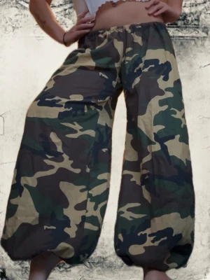 Camo mönstrade vida byxor - Säljer ett par riktigt vida byxor med camo-mönster i grönt, beige och svart. Byxorna har resår i midjan och vid benslut, vilket ger en ballongliknande siluett. Perfekta för dig som vill sticka ut och köra på en streetwear vibe. Materialet ser ut att vara bomull eller bomullsblandning. Passar från 36-42.  Sydda av mig ! 