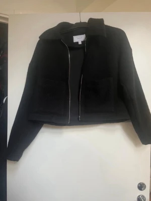 Svart jacka  - Snygg svart cardiganjacka från vila med rak passform och två stora fickor framtill. Jackan har dragkedja. Materialet är mjukt och lite fluffigt, perfekt för lager på lager under kyliga dagar.