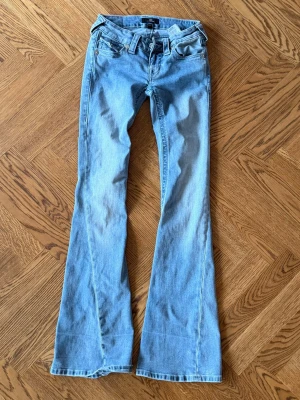 Ljusblå bootcut jeans True religion - Säljer ett par ljusblå bootcut jeans från true religion  med klassisk femficksmodell och normalhög midja. Jeansen har utsvängda ben och är tillverkade i mjuk denim med snygg tvätt. Perfekta för en avslappnad och trendig look.