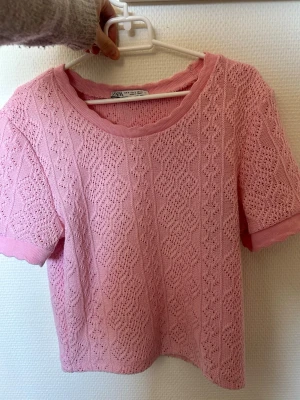 Rosa topp från Zara - Supersöt rosa topp från Zara med korta ärmar och rund hals. Toppen är stickad med ett spetsliknande mönster och har ribbade kanter vid ärmslut och halsringning. 