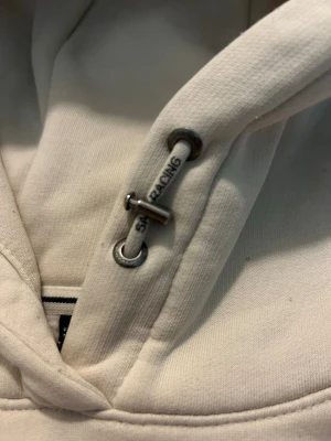Vit hoodie från Sail Racing - Snygg gräddvit hoodie från Sail Racing med justerbar huva. Logga på bröstet och på luvan. Storlek L men skulle mer säga att de är M eller S 