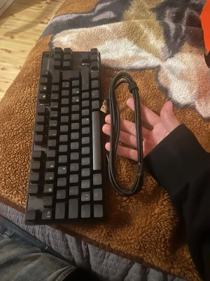 Svart mekaniskt tangentbord USB - Säljer ett svart mekaniskt tangentbord med USB-anslutning. Tangentbordet har en kompakt design och medföljande kabel. På baksidan finns ett fack med ett orange verktyg för att ta bort tangenter. Perfekt för gaming eller skrivarbete.