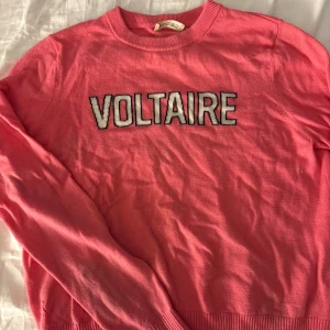 Rosa stickad tröja från Zadig & Voltaire - Cool rosa stickad tröja från Zadig & Voltaire med VOLTAIRE-text i vitt och svart framtill. Tröjan har rund halsringning, långa ärmar och ribbade muddar vid ärmslut och nederkant. Perfekt för dig som gillar statement-plagg och vill sticka ut.