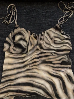 Zebramönstrad topp från Zara - Säljer en zebramönstrad linnetopp från Zara med tunna knytband och lätt transparent material. Toppen har en croppad passform. Supersnygg till både jeans och kjol! Har aldrig använt! 