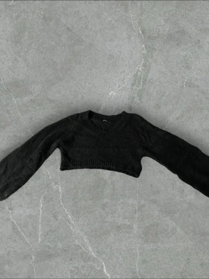 Svart cropped stickad tröja Ginatricot - Trendig svart cropped stickad tröja från Ginatricot med v-ringad hals och långa ärmar. Tröjan har ribbade muddar vid halsringning, ärmslut och nederkant. Perfekt att styla med höga jeans eller kjol för en cool look.