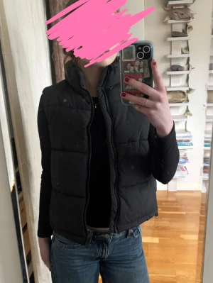 Svart dunväst med hög krage - Snygg svart dunväst med hög krage och dragkedja framtill. Västen har en quiltad design och passar perfekt över en hoodie eller tröja. Enkel och stilren look som funkar till det mesta specielt nu till våren🌸