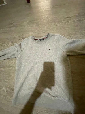 Grå sweatshirt från Tommy Hilfiger - Snygg grå sweatshirt från Tommy Hilfiger med rund halsringning och diskret logga broderad på bröstet. Tröjan har långa ärmar, ribbade muddar och är tillverkad i mjukt sweatshirtmaterial. Perfekt för en avslappnad och stilren look.