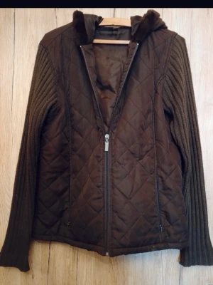 Unik quiltad jacka med stickade ärmar - Jätte cool och trendig brun jacka med stickade ärmar, pälsdetajs och stickad huva. Mitten är quiltad med flis material, perfekt till våren.