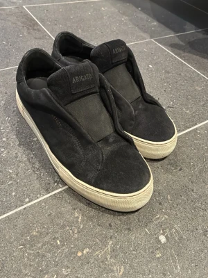 Svarta sneakers från Axel Arigato - Säljer ett par svarta sneakers från Axel Arigato med minimalistisk design. Skorna har en ovandel i mocka och textil, bred elastisk panel över vristen och vit sula. Märkeslogga på plösen och sidan. Perfekta för en clean och stilren look. Perfekta skor inför våren och sommaren😁😉