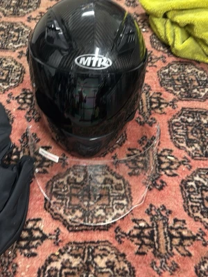 Svart MTR integralhjälm kolfiber - Säljer en svart integralhjälm från MTR i kolfiber-look. Hjälmen har en blank finish och medföljer ett extra visir i klart material. Perfekt för dig som vill ha en snygg och lätt hjälm till motorcykel eller moped.