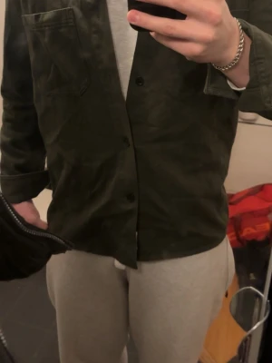 Mörkgrön overshirt från ARKET - Stilren mörkgrön overshirt med knäppning framtill och bröstficka. Overshirten har en rak passform och är i storlek 52 som är m/l