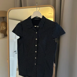 Svart prickig kortärmad skjorta - Kortärmad skjorta i svart med vita prickar. Supersnygg till sommaren. Från brandy mellville. Den är helt oanvänd. Passar mig som brukar ha M och S på tröjor. 
