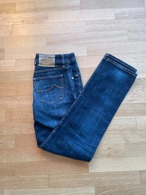 Jacob Cohën Straight Fit Jeans - Jacob Cohën straight fit jeans i marinblå/blå. Mycket bra skick, använda ett fåtal gånger och har ett mycket bra helhetsintryck. Mått: midja ca 39 cm, längd ca 106 cm. Material: 100% bomull. Säljes som de är. Skickas välpackade inom 24 timmar.