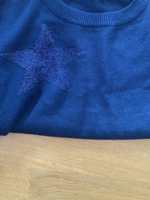 Mörkblå tunn stickad tröja med stjärnor - Snygg mörkblå stickad tröja med glittriga stjärnor på bröstet och nedtill. Tröjan har rund halsringning och långa ärmar. Perfekt för dig som gillar en cool och avslappnad stil.
