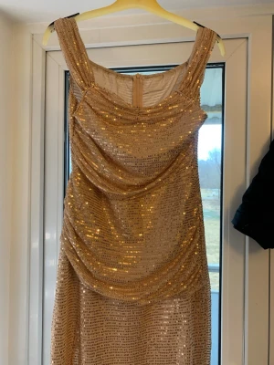 Glittrig champagnefärgad klänning - Snygg glittrigande klänning i champagnefärg med paljetter och draperad front. Klänningen har breda axelband och en smickrande passform som ger en elegant look.  Perfekt för dig som vill sticka ut med stil💃✨👀