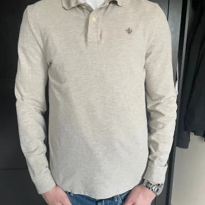 Beige långärmad skjorta Morris - Säljer en stilren beige långärmad Piké från Morris med klassisk krage och diskret logga nu på bröstet. Skjortan är tillverkad i mjuk bomull och har knappar framtill. Perfekt för dig som gillar enkel och clean stil.