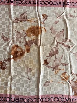 Roccobarocco vintage halsduk i siden - Lyxig halsduk från Roccobarocco i beige med rosa kant och mörkblå logotyp längs kanten. Har blommigt mönster i bruna och rosa toner samt diskret rutmönster i bakgrunden. Perfekt accessoar för att lyfta din outfit. 100% siden, perfekt skick. Mått 90x90