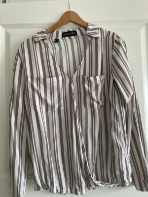 Randig blus från Bodyflirt - Snygg blus med beige och vita vertikala ränder från Bodyflirt. Modellen har v-ringning, krage, två bröstfickor och långa ärmar. Materialet känns lätt och luftigt, perfekt för en trendig look. Använd i 2 gånger