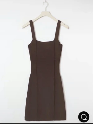 Brun tight kortklänning med breda axelband - En stilren brun kortklänning med breda axelband och figurnära passform. Klänningen har en enkel design utan mönster och markerade sömmar framtill som ger en snygg siluett. Perfekt för dig som gillar minimalistisk stil.