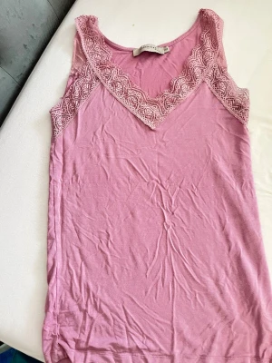 Rosa spetsdetaljerad linnetopp - Söt rosa linnetopp från Essential by Vero Moda med v-ringning och breda spetsdetaljer längs halsringningen och axlarna. Toppen är ärmlös och har en mjuk, bekväm känsla som passar perfekt till sommaren.